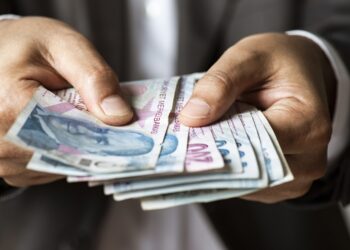 Man in suit holding hundred and two hundred Turkish Lira banknotes.