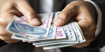 Man in suit holding hundred and two hundred Turkish Lira banknotes.
